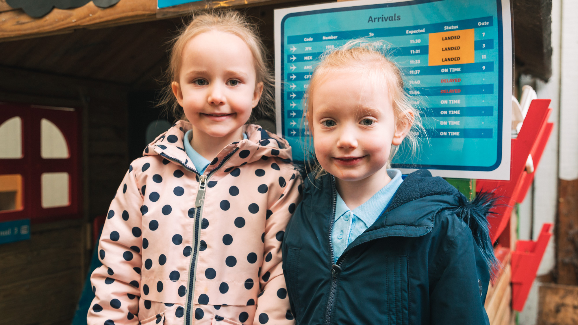 Two nursery pupils stand in front of the camera and smile.